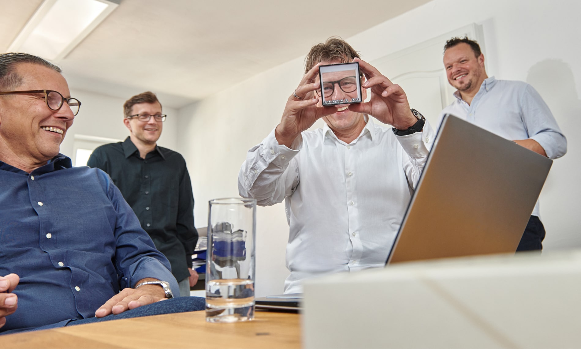 Claus Seitz, Andre Herzog, Detlef Westenberger und Sebastian Arnold sitzen nebeneinander lachend vor einem Laptop